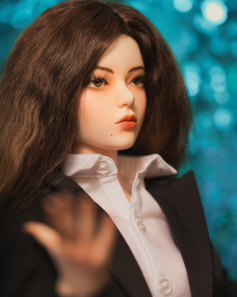 A female doll with long brown hair wearing a white button up shirt with a black blazer