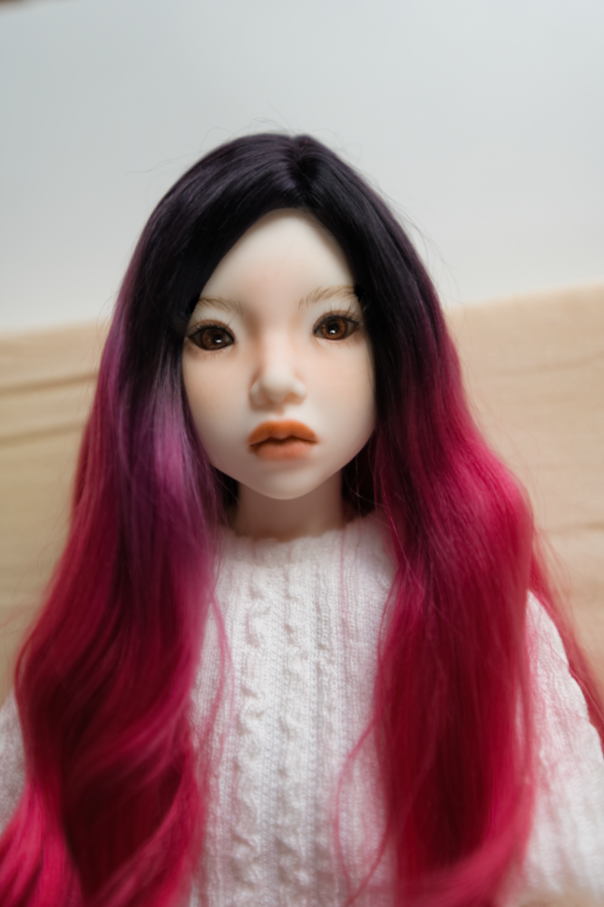 A child female doll with red and black hair wearing a white cable knit sweater